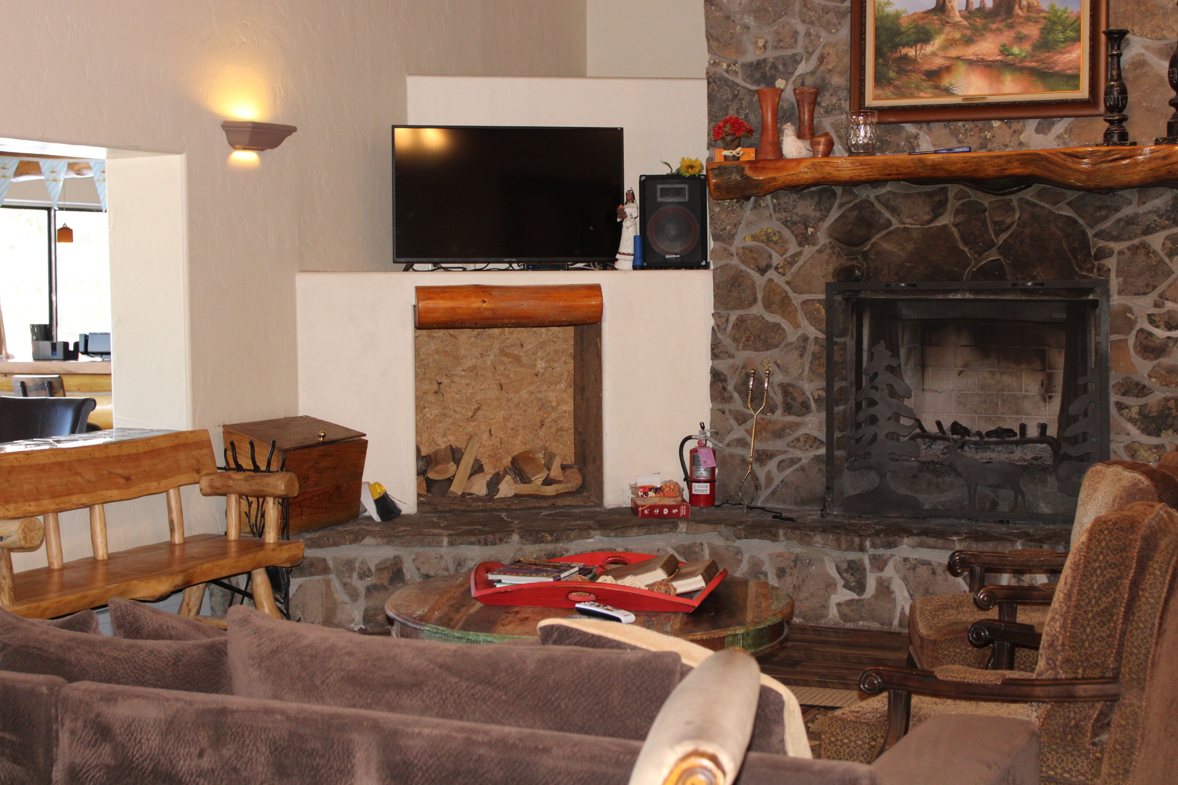 A cozy living room with a stone fireplace, a flat-screen TV, and a wooden bench.