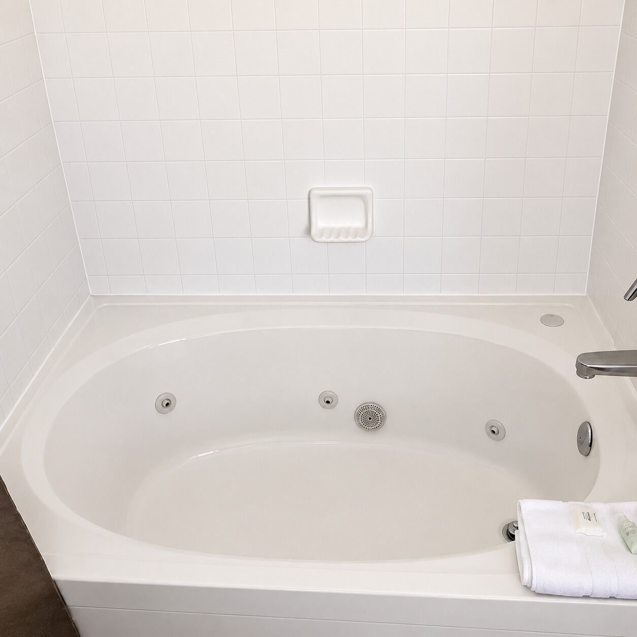 Een wit bad met een ingebouwd zeepbakje, een handdoek en een handdouche.