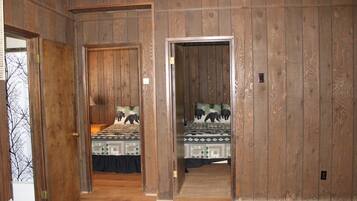 A room with wooden panel walls, two beds with patterned bedding, and a rug on the floor.