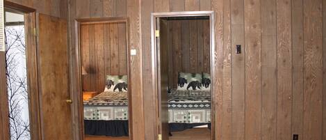 A room with wooden panel walls, two beds with patterned bedding, and a rug on the floor.