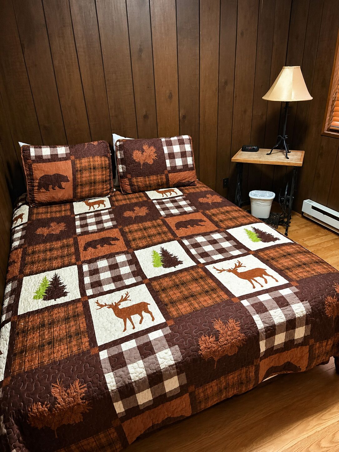 Ein Bett mit karierter Decke mit Tiermotiven, ein Nachttisch mit Lampe und ein Holzboden.