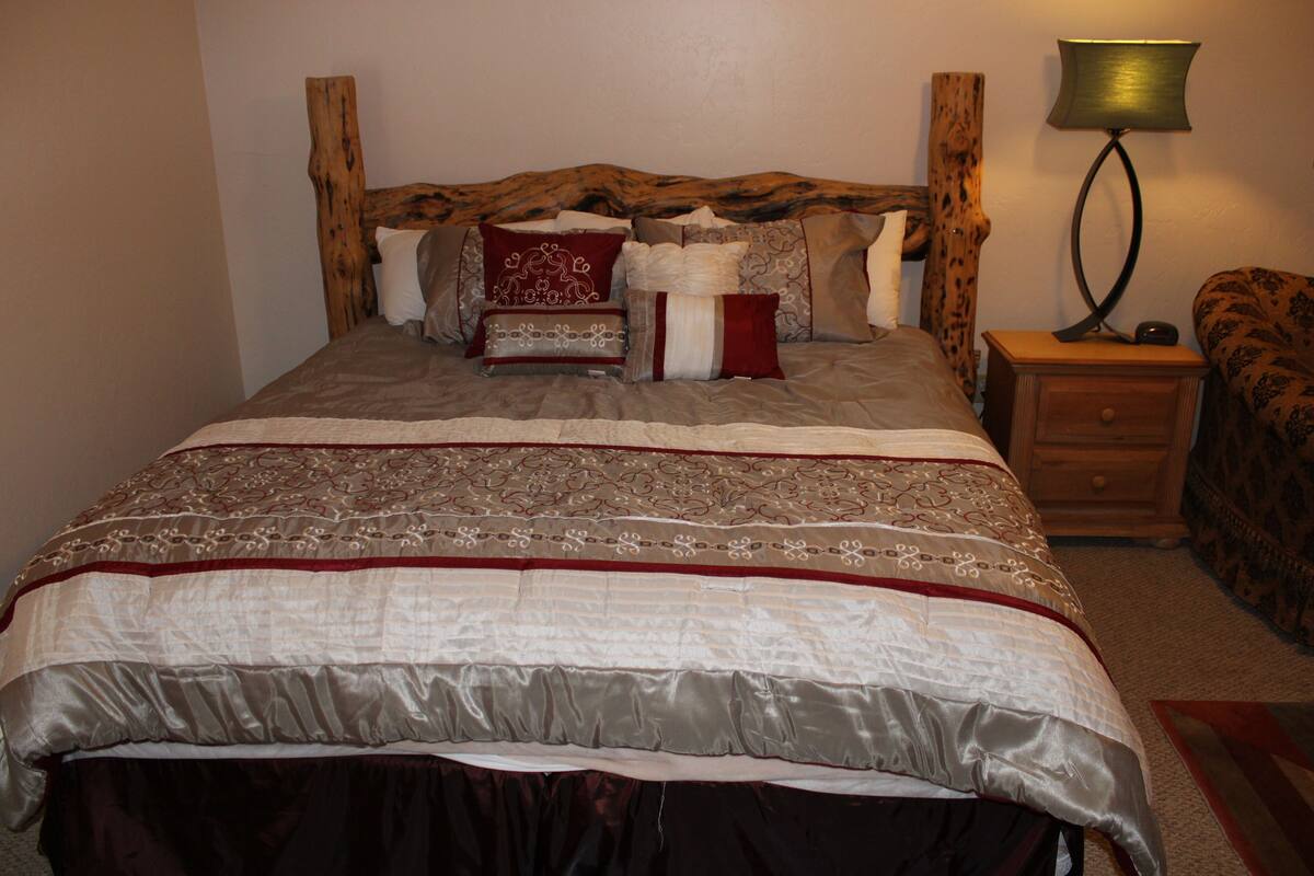 A bed with a wooden headboard, a bedside table with a lamp, and a patterned throw blanket.