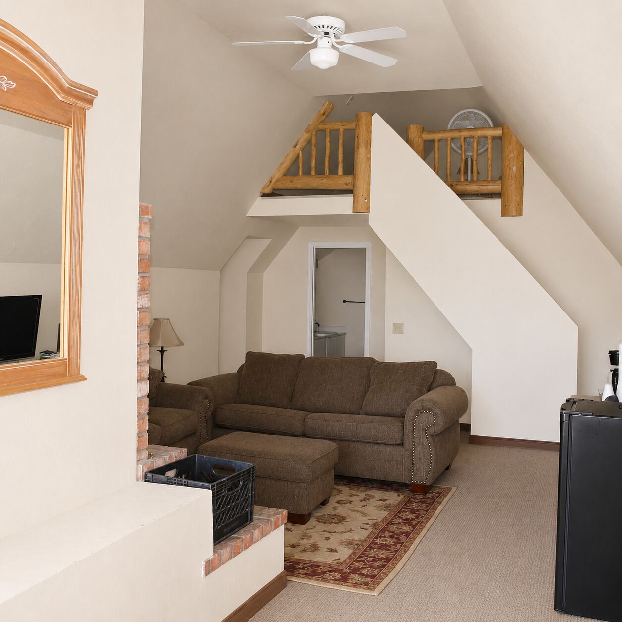 A loft-style room with a sofa, a small table, a ceiling fan, and a staircase.
