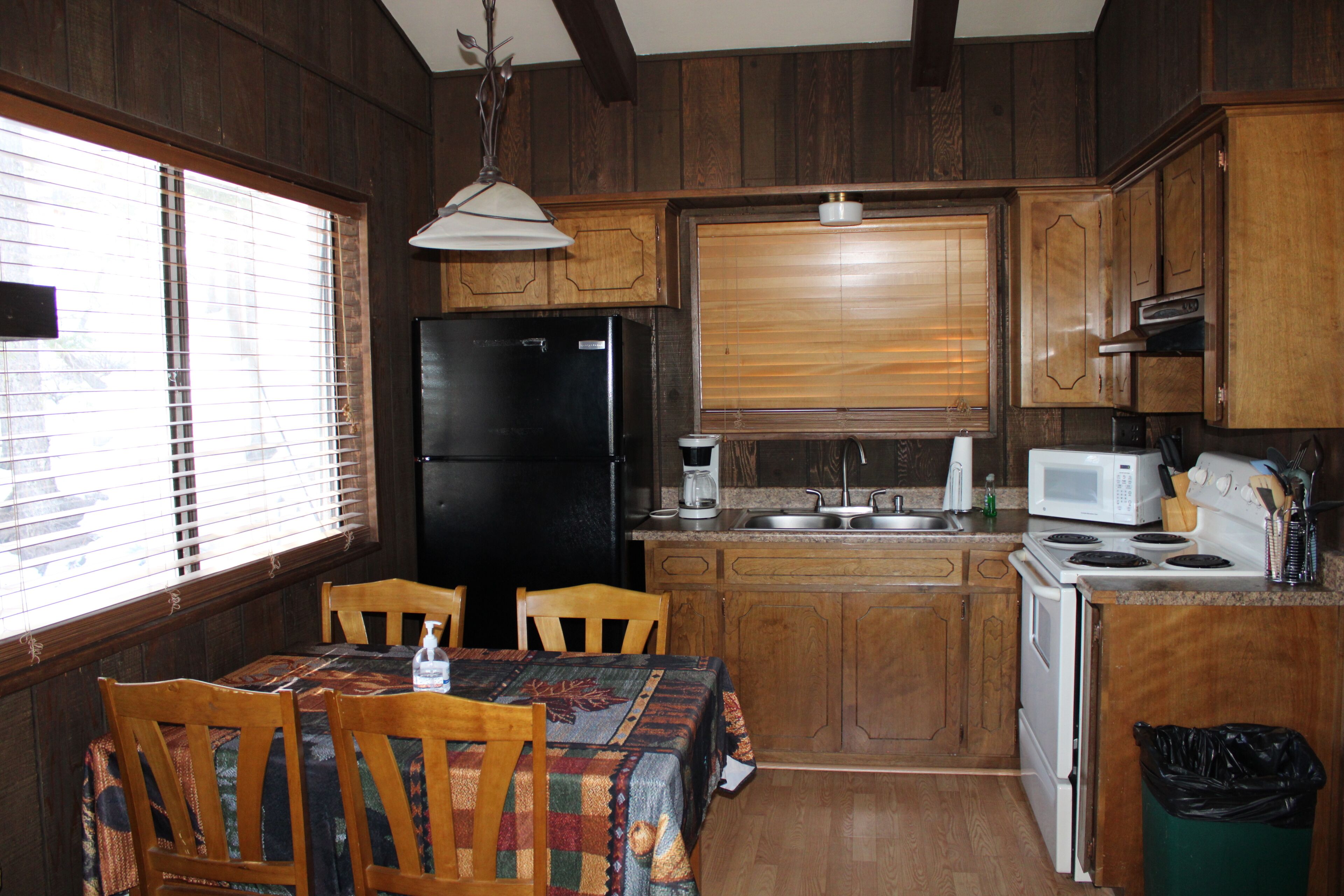 A kitchen with wooden cabinets, a black refrigerator, a microwave, a stove, and a dining table with chairs.
