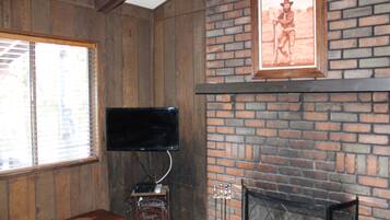 Une pièce aux murs en bois, avec une cheminée en briques, un téléviseur fixé au mur et un tableau encadré au-dessus de la cheminée.