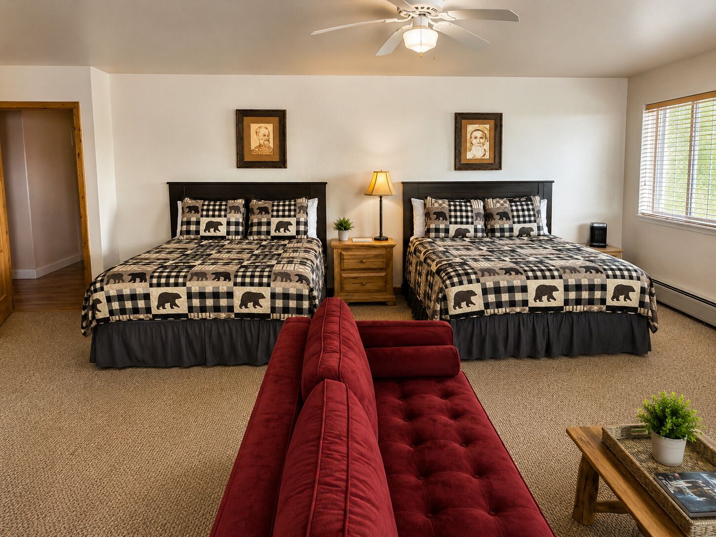 A bedroom with two beds, a red sofa, a ceiling fan, and a window with blinds.