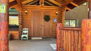 Una baita di legno con un portico in legno, una doppia porta decorata con una ghirlanda, un cartello con la scritta 'No servizi igienici pubblici' e un cartello con l'avvertenza 'Attenzione a ghiaccio e neve che cadono'.