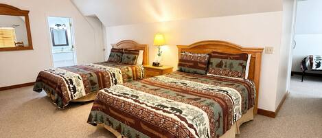 A bedroom with two beds, a nightstand with a lamp, a mirror, and a door leading to a bathroom.