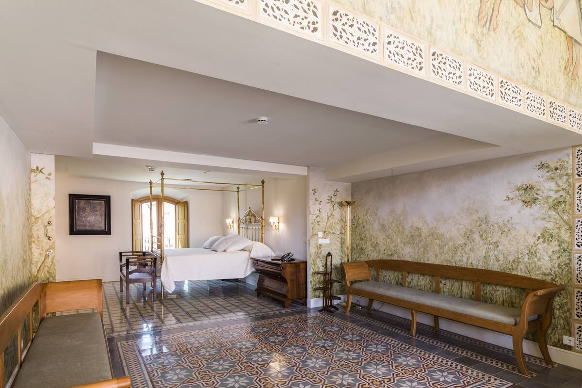 Quarto com uma cama de dossel, um banco de madeira, piso estampado e parede decorativa.