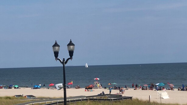 A beach with a clear sky, a sailboat in the distance, and a lifeguard tower.