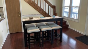 A kitchen with a wooden staircase, a dining table with four barstools, and a window with a view.