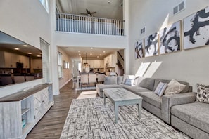 A spacious living area with a high ceiling, a balcony, a kitchen, and a dining area.