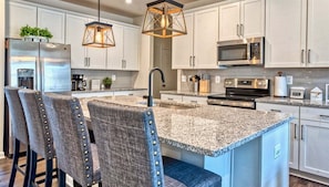 A modern kitchen with granite countertops, stainless steel appliances, and bar stools.