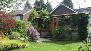 A residential garden with a wooden pergola, a brick house, and various shrubs.