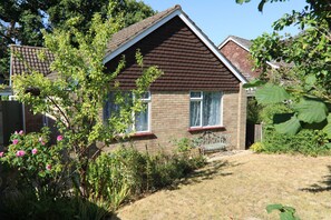A house with a brick exterior, a brown roof, and a front yard with a bench and flowering plants.