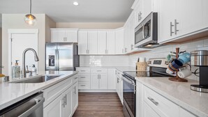 Una cocina moderna con armarios blancos, electrodomésticos de acero inoxidable y suelo de madera.