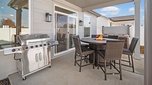 Un patio exterior con una parrilla de acero inoxidable, sillas de mimbre y una mesa con chimenea.