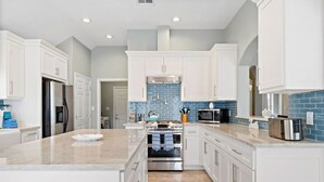 Una cocina moderna con armarios blancos, una isla central, electrodomésticos de acero inoxidable y salpicadero con azulejos azules.
