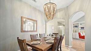 Un comedor con una mesa de madera dispuesta para seis personas, rodeada por seis sillas. Un espejo grande cuelga de la pared sobre la mesa.