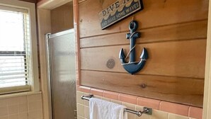 A bathroom with a wooden wall, a towel rack, a sign that says "Dive In and Make Some Waves", and a stainless steel door.