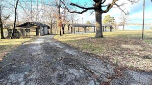 A gravel path leading to a building with a covered porch, surrounded by trees and a clear sky.