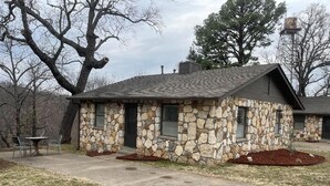 A stone building with a sloped roof, a small porch, and a fire pit area.