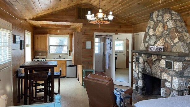 A rustic cabin interior with a stone fireplace, wooden ceiling, and a dining area.