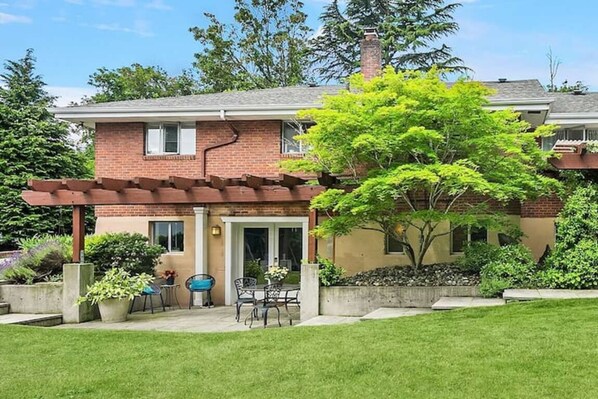 A two-story house with a brick exterior, a covered patio with outdoor furniture, and a well-maintained lawn.