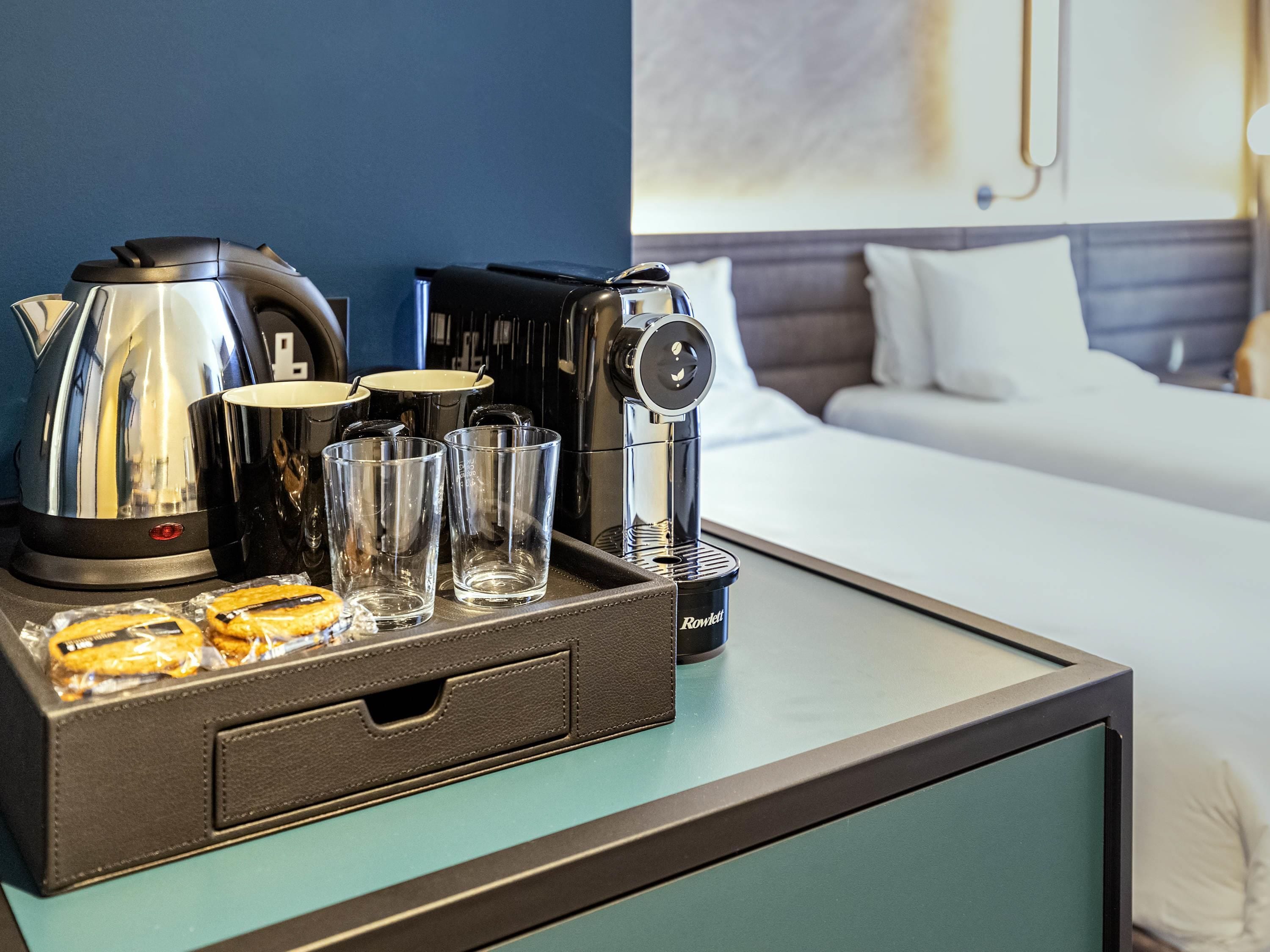 Ein Hotelzimmer mit Bett, Nachttisch mit Serviertablett, Kaffeemaschine, Wasserkocher und Toaster.