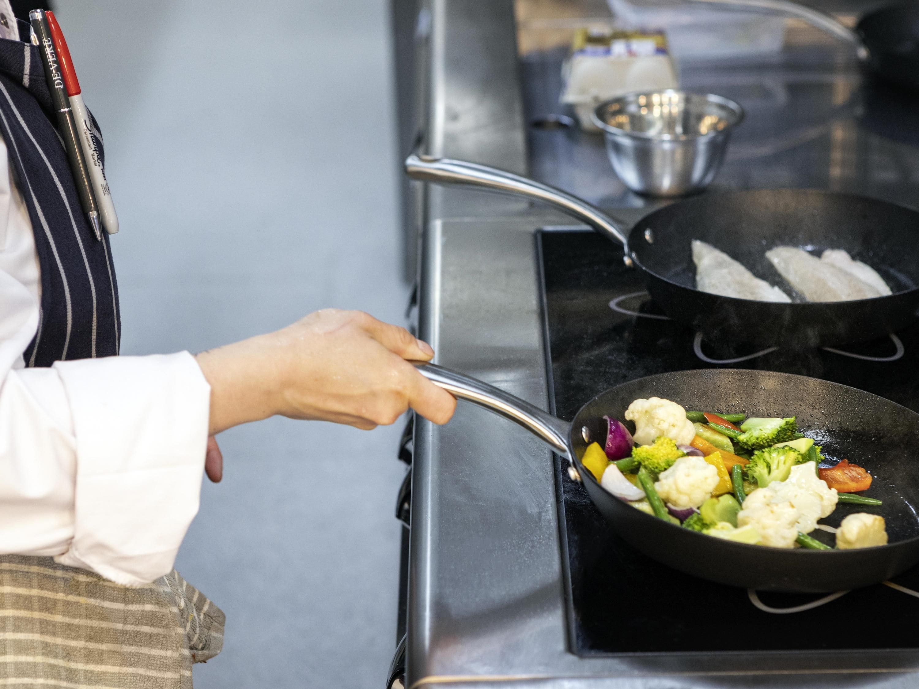 A person cooking vegetables in a pan on a stove.