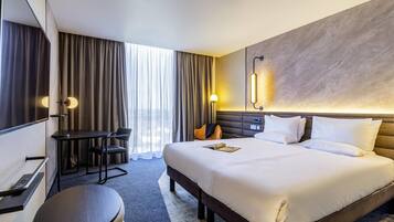 Una habitación de hotel con una cama grande, un escritorio, una silla y un pequeño reposapiés.