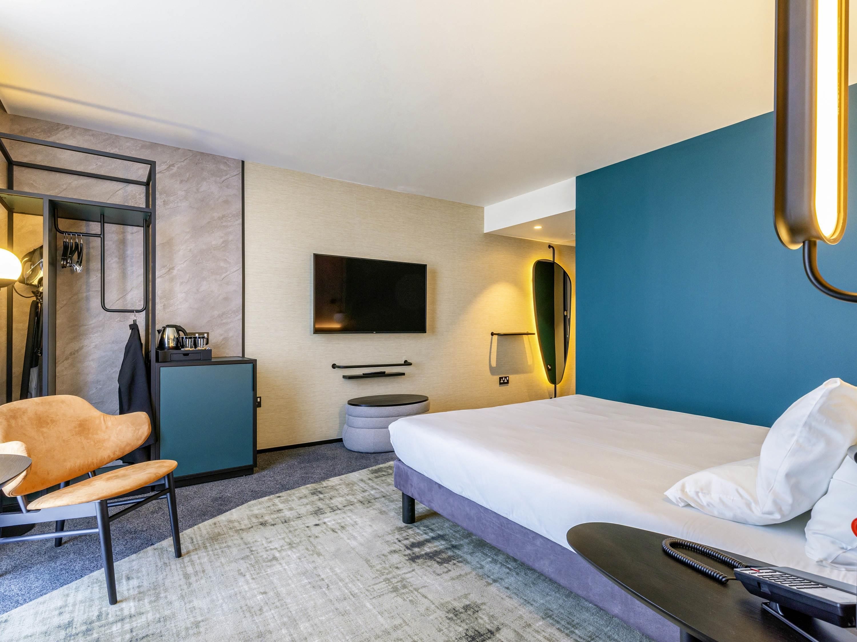 A hotel room with a bed, a desk, a chair, a TV, and a mirror.