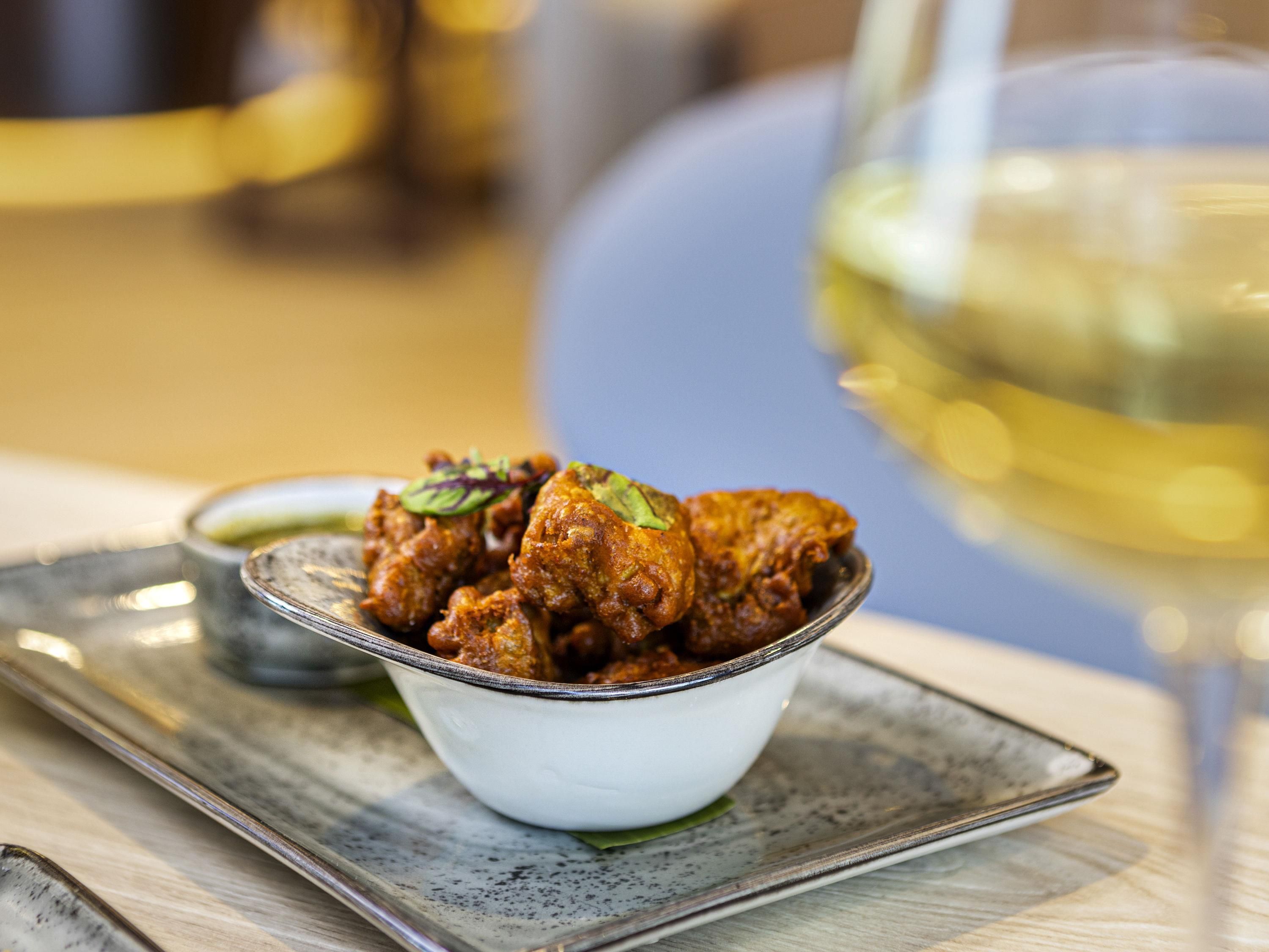 A bowl of food on a plate with a glass of white wine in the background.