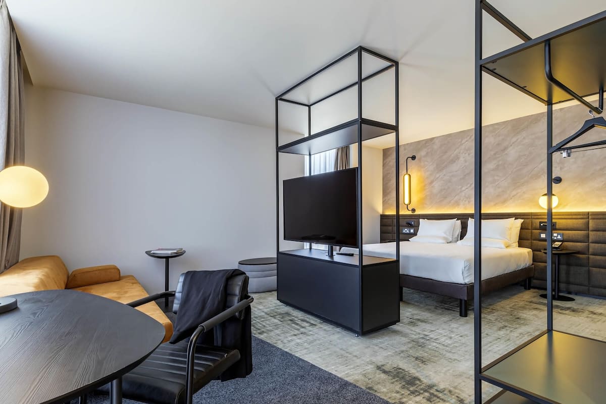 Una habitación de hotel moderna con una cama, un escritorio, una silla, un televisor y un separador de vidrio.
