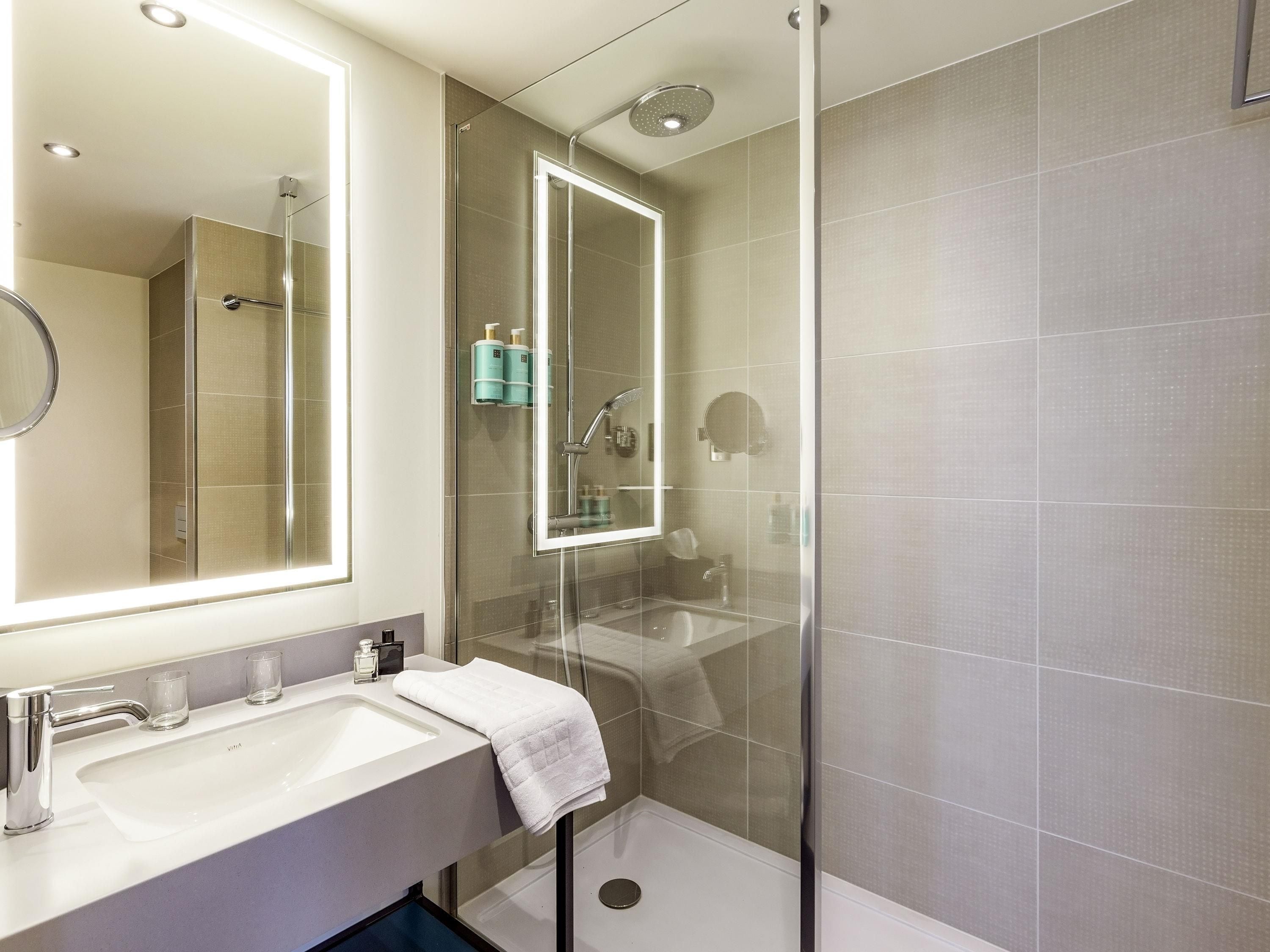 A modern bathroom with a glass-enclosed shower, a large mirror, and a white sink with a towel.