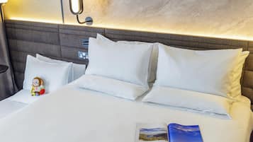 A neatly made bed with white bedding, a plush headboard, and a small plush toy on the pillow.