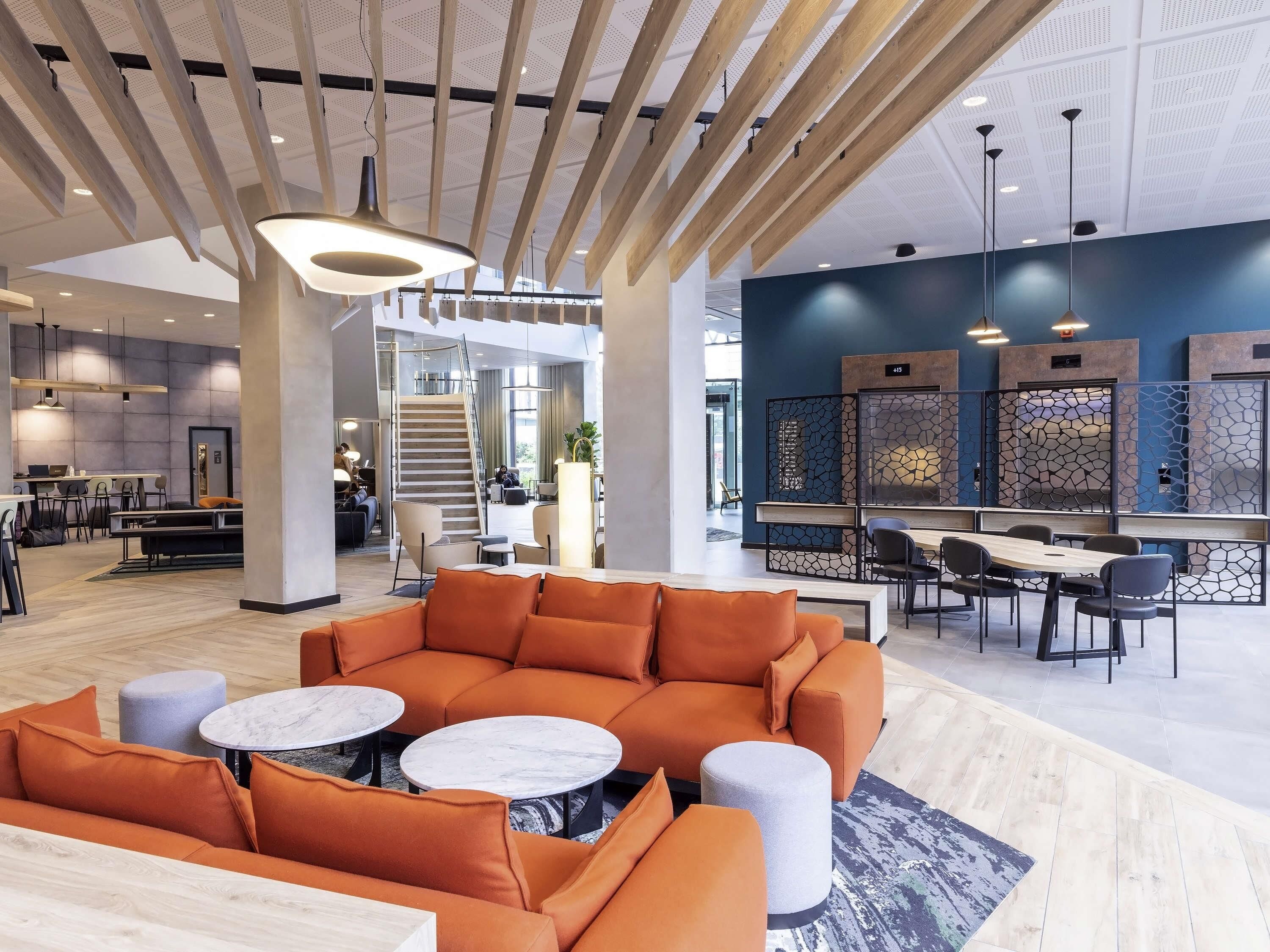 Un vestíbulo de hotel moderno con una zona de estar central, una escalera y una recepción.