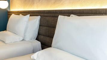 Una habitación de hotel con un cabecero grande y acolchado, y dos camas blancas con almohadas a juego.