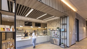 A modern cafe interior with a wooden ceiling, a central counter, and shelves stocked with products. - Novotel Liverpool Paddington Village (Liverpool)