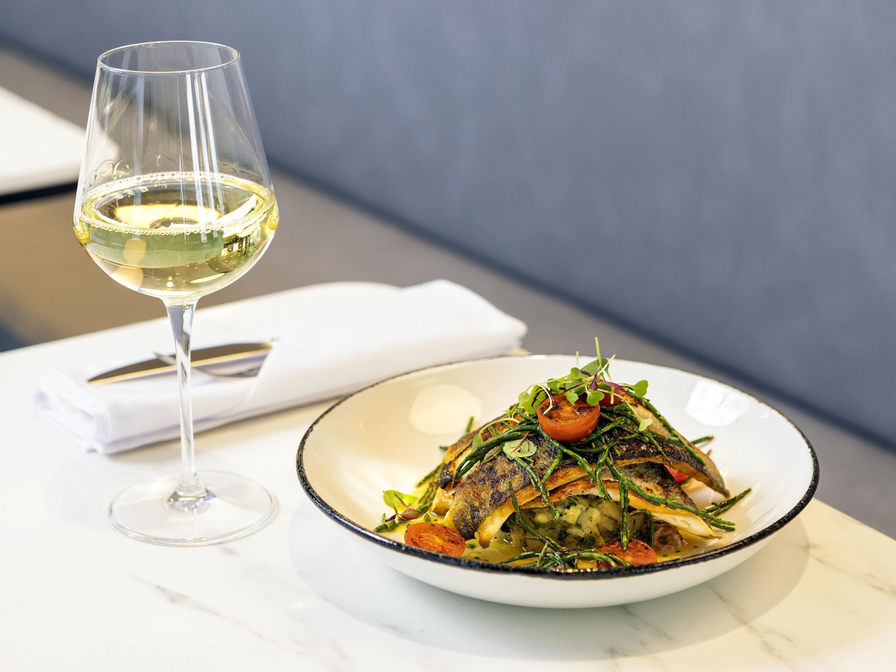 A plate of food with a glass of white wine on a table.