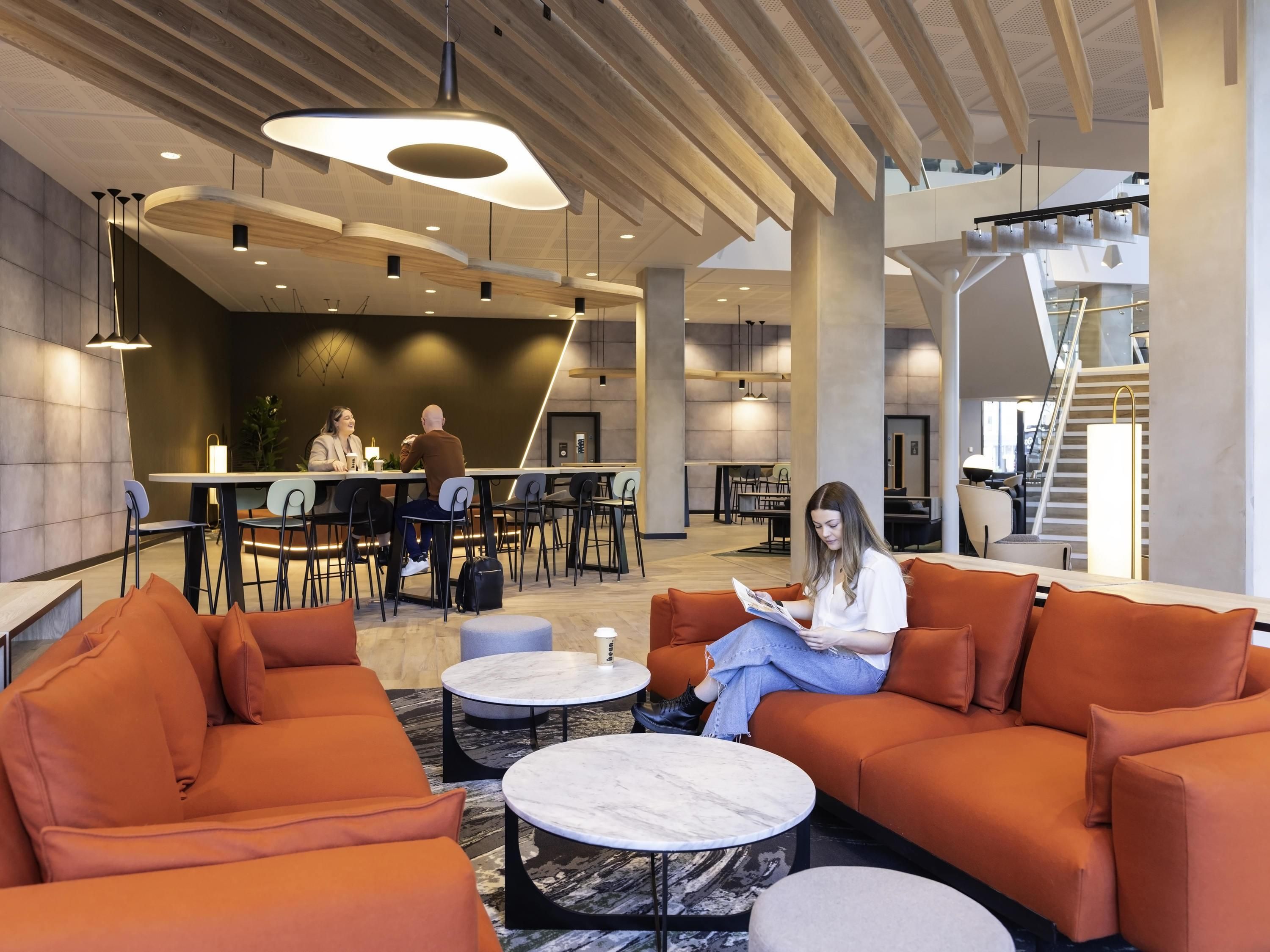 Eine moderne Lobby mit orangefarbenen Sitzgelegenheiten, Marmortischen und einer zentralen Bar.