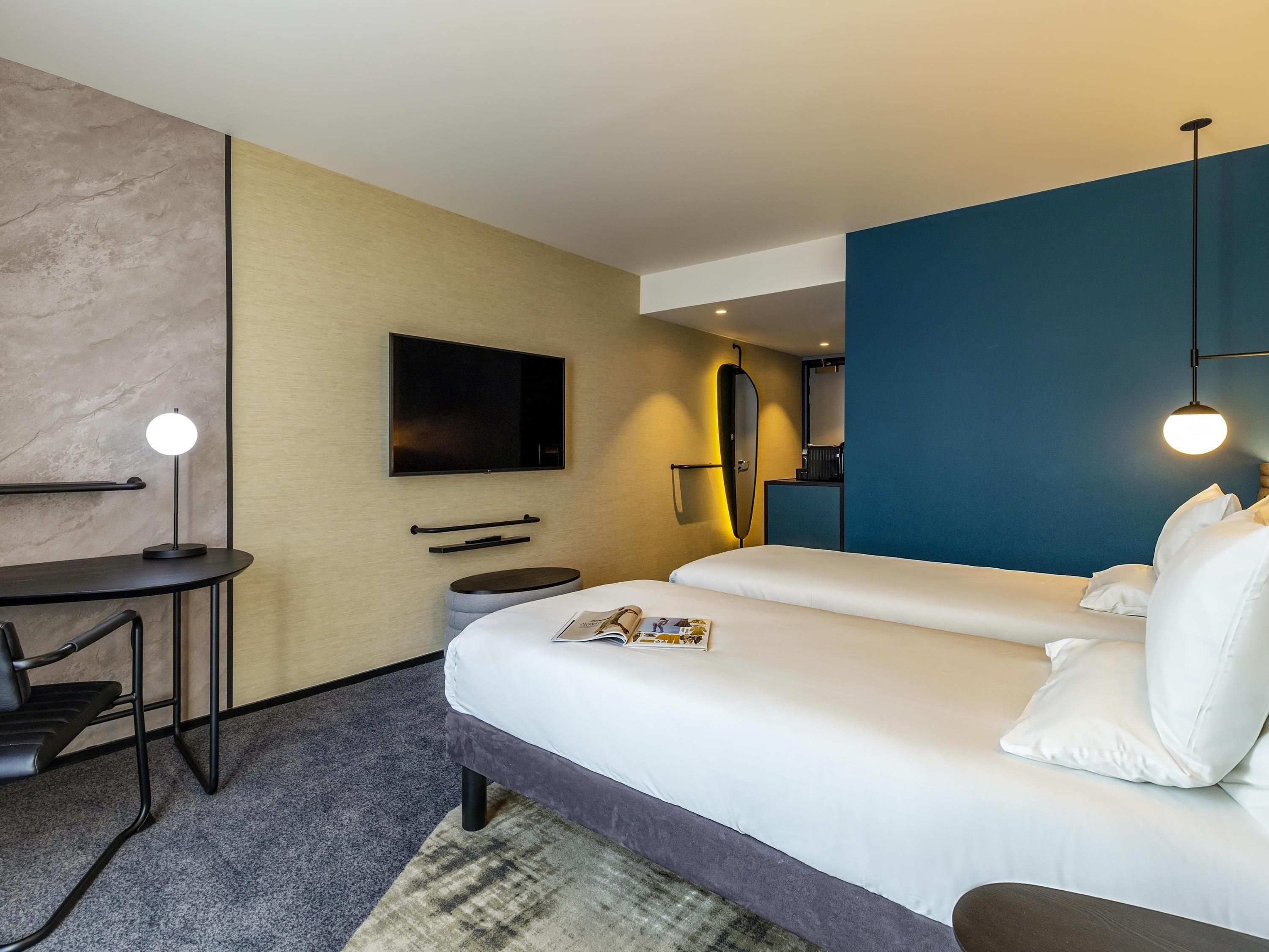 Una habitación de hotel con cama, mesita de noche, lámpara, televisión y un escritorio con silla.
