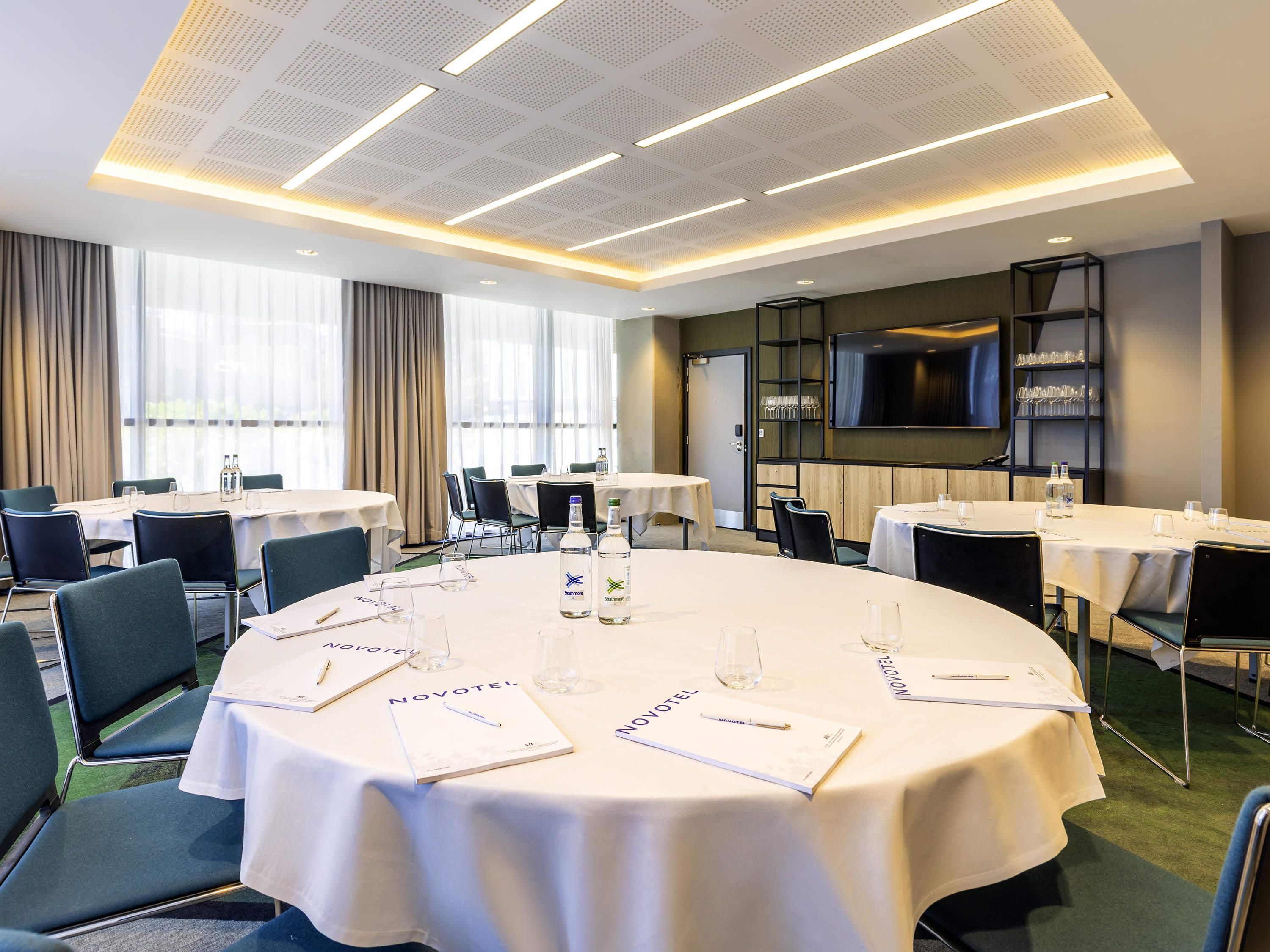 A conference room with round tables, chairs, and a television on the wall.