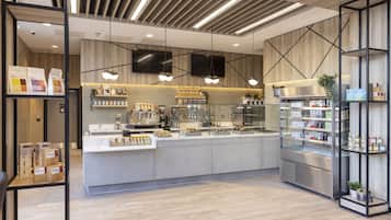 Un café moderno con mostrador central, estanterías con productos envasados y una vitrina refrigerada.