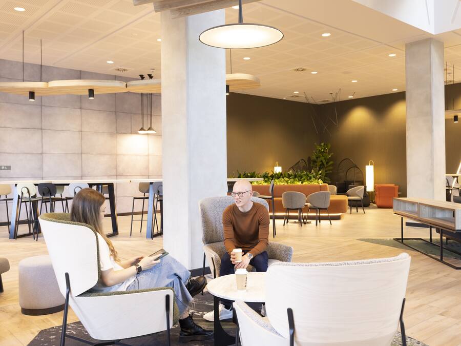 Uma área de estar moderna, com assentos, uma mesa de centro e uma planta grande.