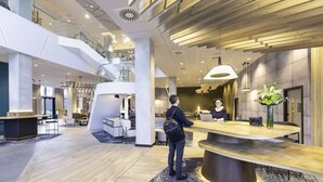 A modern hotel lobby with a reception desk, seating area, and a staircase leading to an upper level.