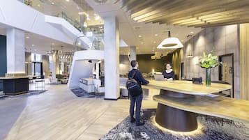 Un moderno vestíbulo de hotel con mostrador de recepción, zona de estar y una escalera que conduce a un nivel superior.