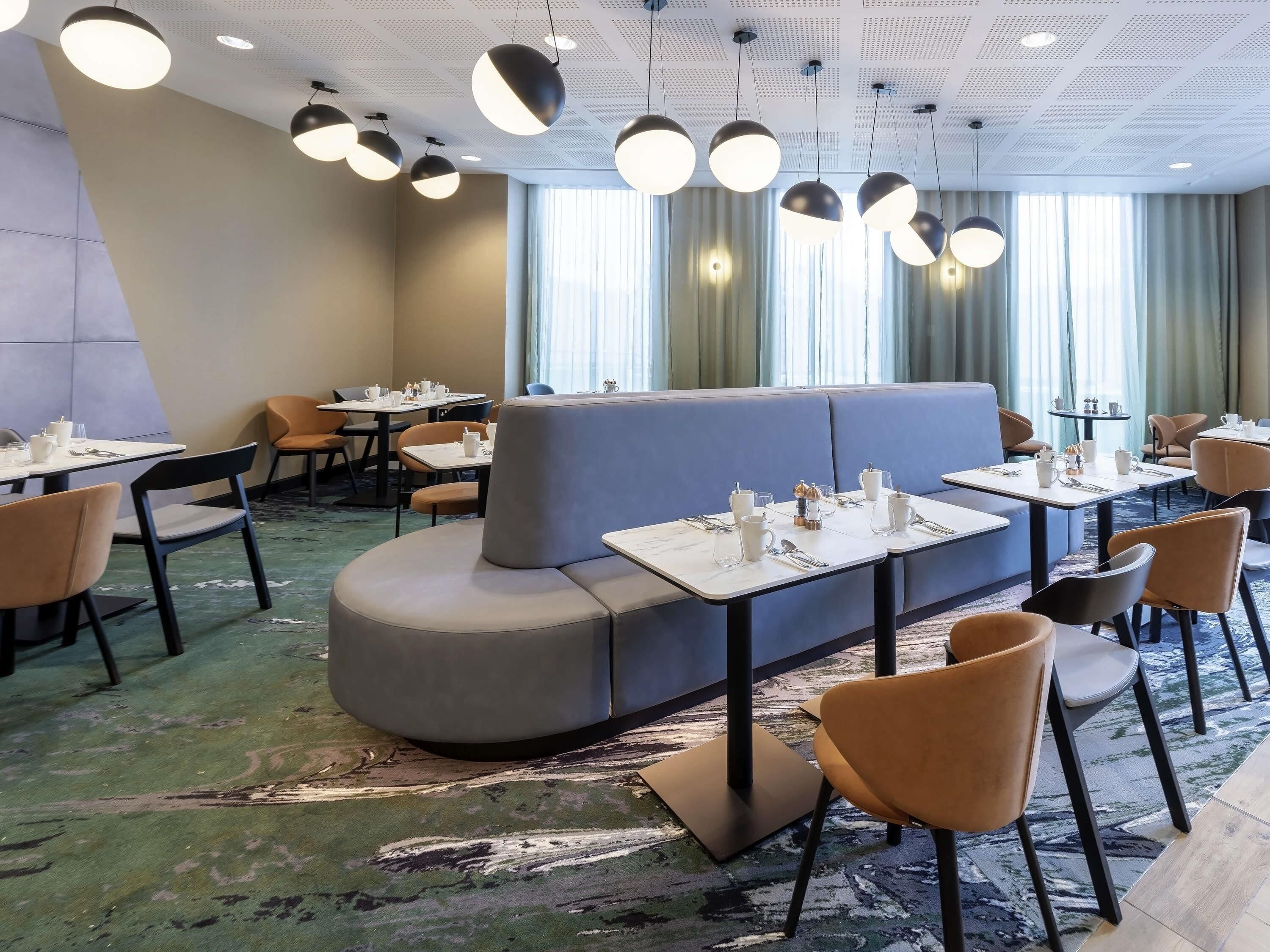 A modern dining area with round tables, cushioned seating, and pendant lighting.