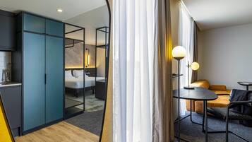 A modern hotel room with a bed, bedside table, lamp, and a seating area with a table and chairs.