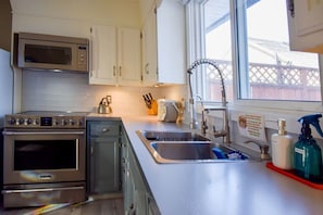A kitchen with stainless steel appliances, a double sink, and a window with a view of a fence.